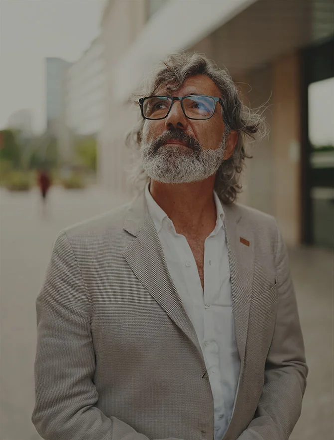 A man with glasses and a gray beard looks upward while standing outside a building. He wears a light-colored blazer and white shirt. - Home, Webster, TX