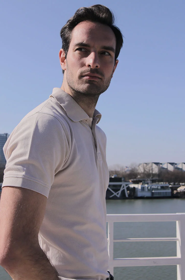 A young to middle-aged man wearing a white beige collared short-sleeve shirt, looking past the camera. He has brown hair and a slight beard, standing in front of a pier. - Procedures Treatment in Webster, TX