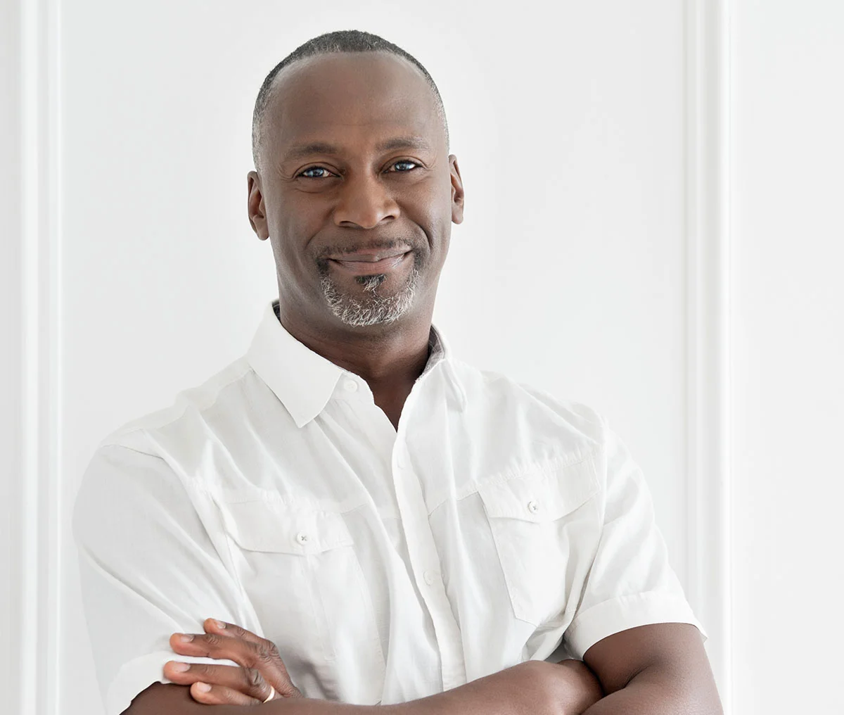Portrait of a middle to older-aged man with grey hair, wearing a beige blazer over a white shirt. He stands in an architecturally styled background, looking at the camera with a gentle smile, which adds warmth to the composition. - Types of Kidney Stones in Webster, TX