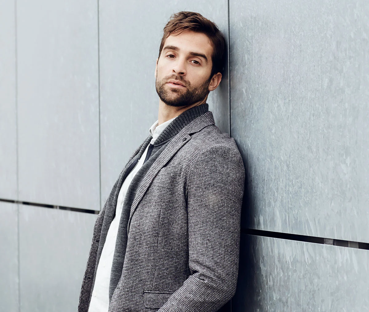 Man in a grey blazer leaning against a wall. - Vasectomy in Webster, TX